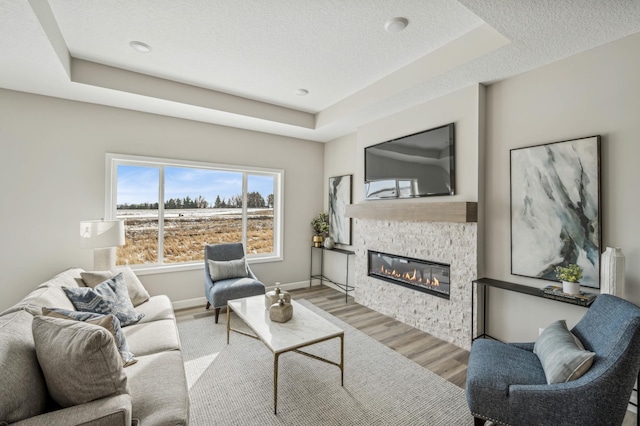 living room featuring a tray ceiling, a stone fireplace, a textured ceiling, and light wood-type flooring