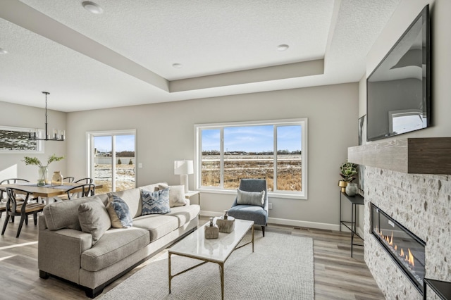 living room featuring light hardwood / wood-style flooring, a textured ceiling, a fireplace, and a tray ceiling