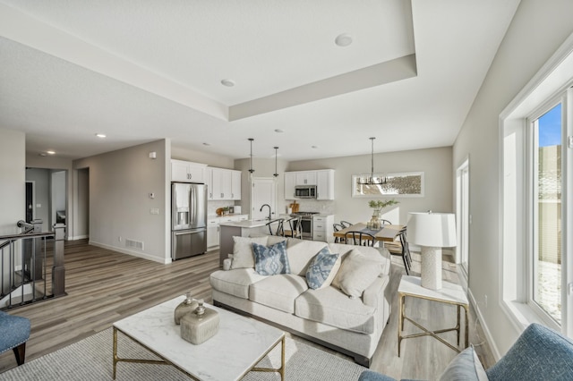 living room with a raised ceiling, plenty of natural light, sink, and light hardwood / wood-style flooring