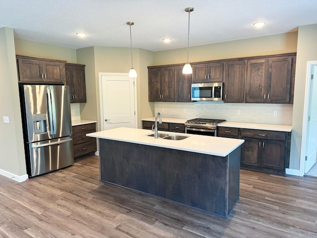 kitchen with stainless steel appliances, hanging light fixtures, a kitchen island with sink, and dark brown cabinetry