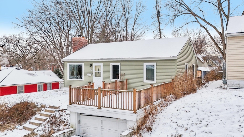 snow covered back of property featuring a garage and a deck