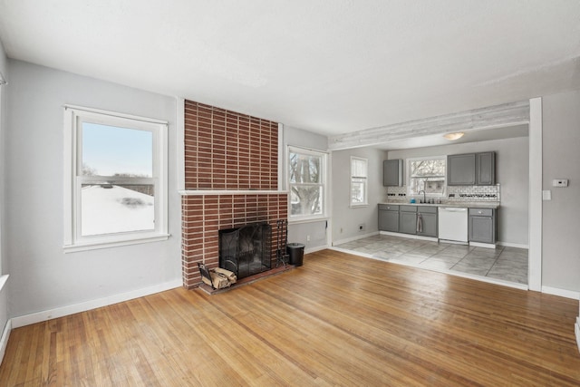 unfurnished living room with sink, a tile fireplace, and light hardwood / wood-style floors