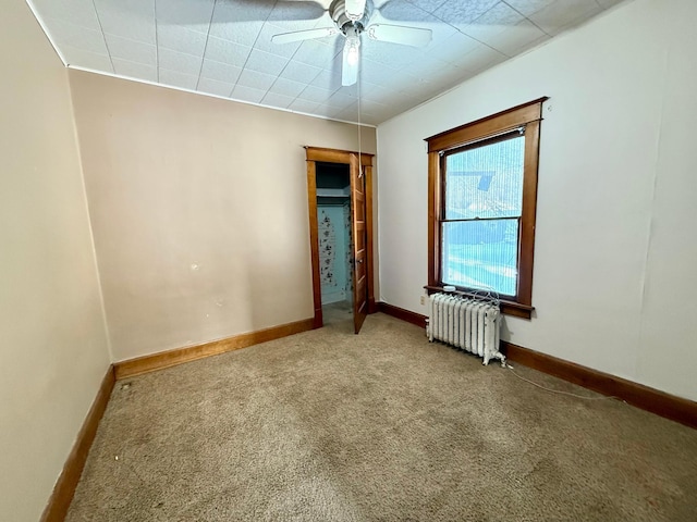 unfurnished room with carpet flooring, ceiling fan, and radiator heating unit