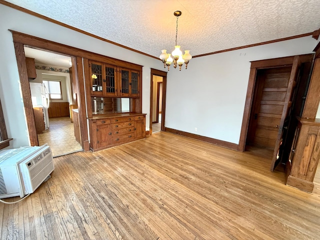 unfurnished dining area featuring a wall mounted AC, light hardwood / wood-style flooring, a textured ceiling, and an inviting chandelier