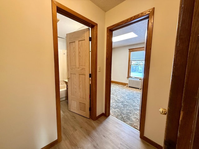 hall featuring radiator heating unit, a textured ceiling, and light wood-type flooring