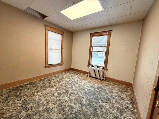 unfurnished room with radiator, a drop ceiling, and carpet