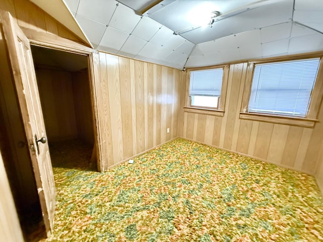 empty room featuring carpet floors, vaulted ceiling, and wooden walls