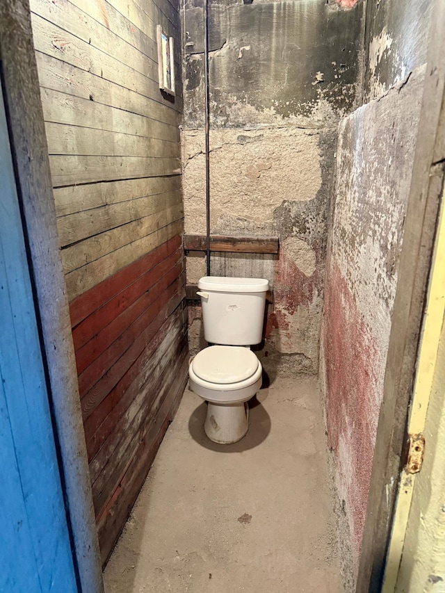 bathroom with concrete floors, toilet, and wood walls