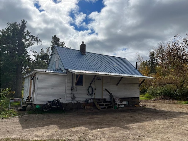 back of house with entry steps, a chimney, and metal roof
