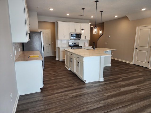 kitchen with decorative light fixtures, dark hardwood / wood-style floors, a center island with sink, white cabinetry, and stainless steel appliances