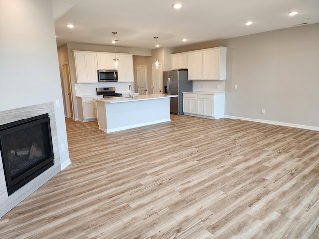 kitchen featuring hanging light fixtures, light hardwood / wood-style floors, a center island with sink, white cabinets, and appliances with stainless steel finishes