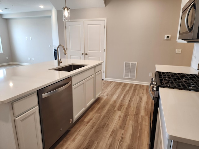 kitchen with sink, stainless steel appliances, light hardwood / wood-style floors, decorative light fixtures, and white cabinets