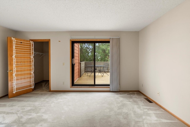 unfurnished bedroom featuring access to exterior, a textured ceiling, light colored carpet, a spacious closet, and a closet