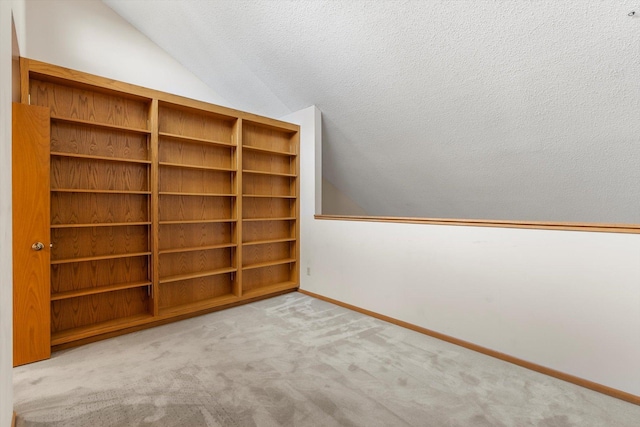 interior space with a textured ceiling, light colored carpet, and vaulted ceiling