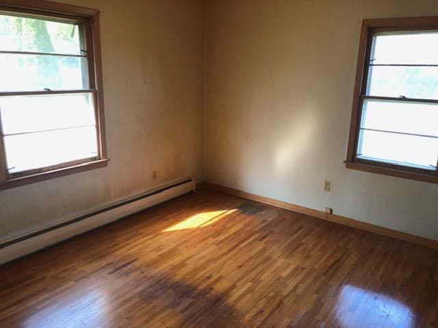 unfurnished room with dark wood-type flooring, plenty of natural light, and a baseboard heating unit