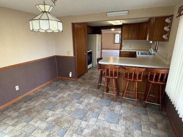 kitchen with kitchen peninsula, a breakfast bar, white appliances, sink, and pendant lighting