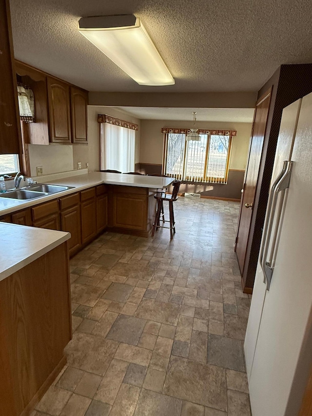 kitchen with kitchen peninsula, a textured ceiling, decorative light fixtures, and sink