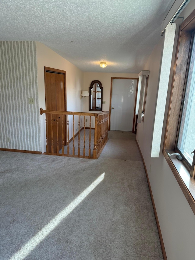 corridor featuring a textured ceiling and light colored carpet