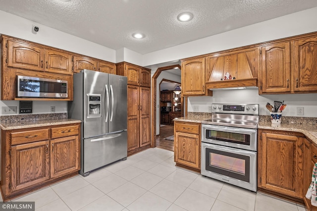 kitchen featuring stone counters, a textured ceiling, stainless steel appliances, and light tile patterned flooring