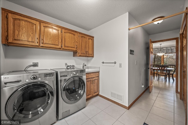 washroom with washer and dryer, light tile patterned floors, cabinets, and a textured ceiling