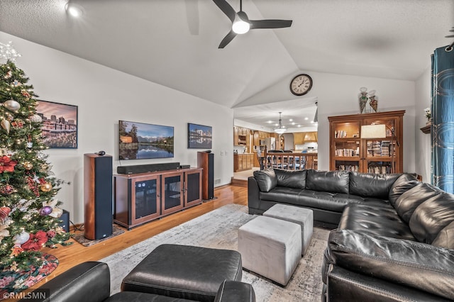 living room featuring ceiling fan with notable chandelier, vaulted ceiling, and light wood-type flooring