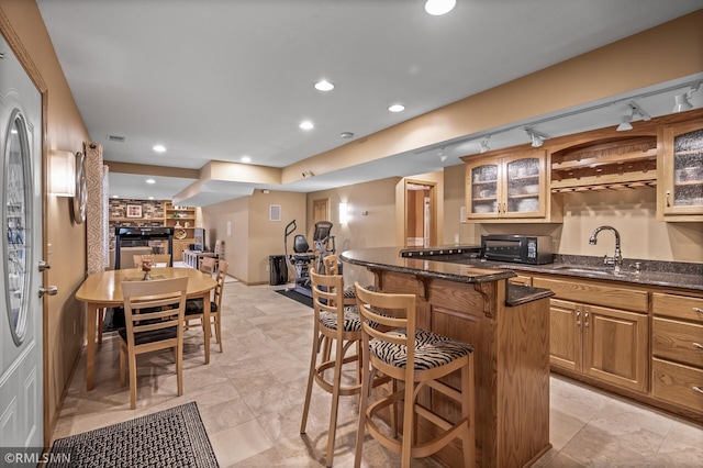 kitchen with rail lighting, sink, dark stone countertops, a kitchen island, and a kitchen bar