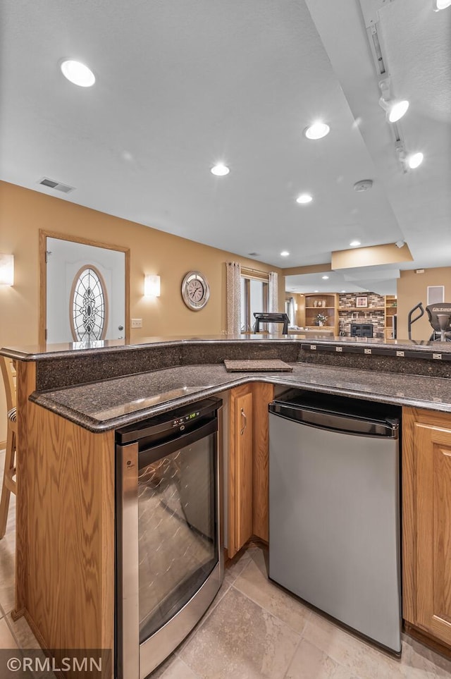 kitchen with dark stone counters, track lighting, wine cooler, stainless steel dishwasher, and kitchen peninsula