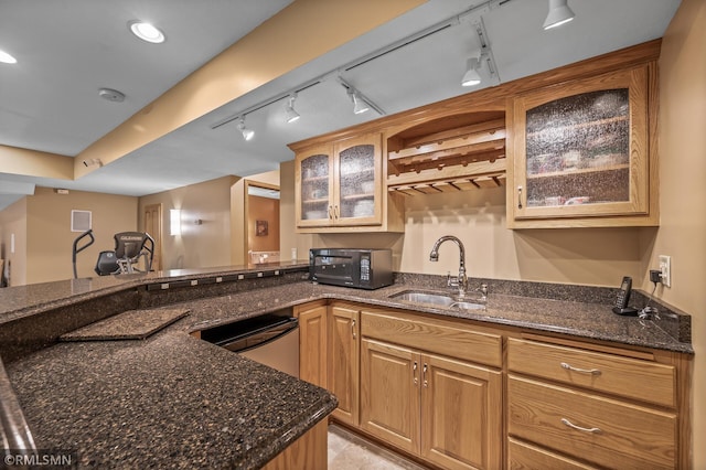 kitchen with kitchen peninsula, rail lighting, sink, dark stone countertops, and dishwasher