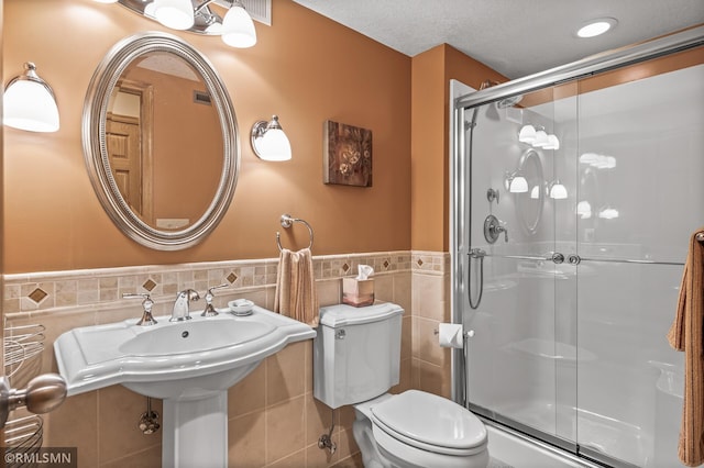 bathroom with a textured ceiling, toilet, tile walls, and walk in shower