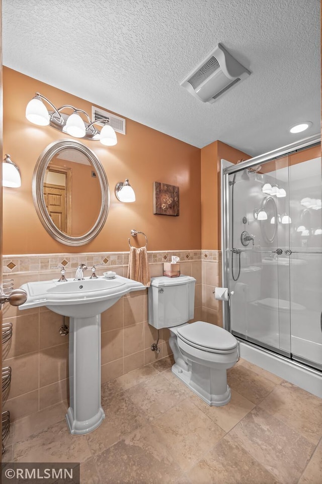 bathroom featuring a textured ceiling, toilet, tile walls, and walk in shower