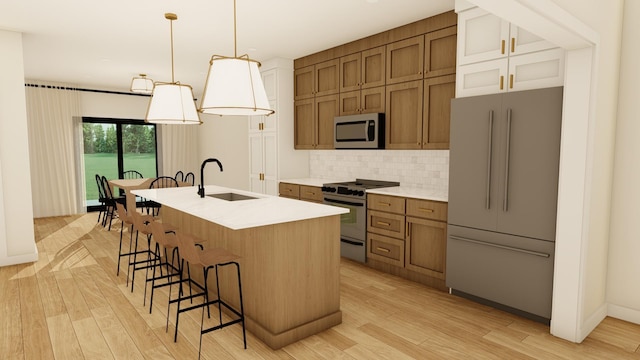 kitchen featuring sink, hanging light fixtures, stainless steel appliances, a center island with sink, and light wood-type flooring