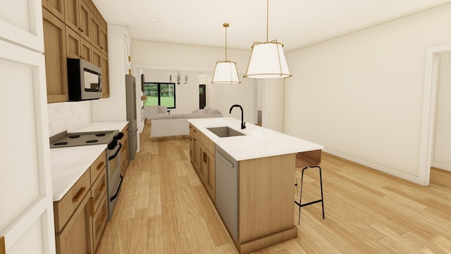 kitchen featuring sink, hanging light fixtures, light hardwood / wood-style floors, a kitchen island with sink, and appliances with stainless steel finishes