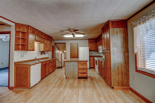 kitchen with a ceiling fan, a sink, a kitchen island, white appliances, and light wood finished floors