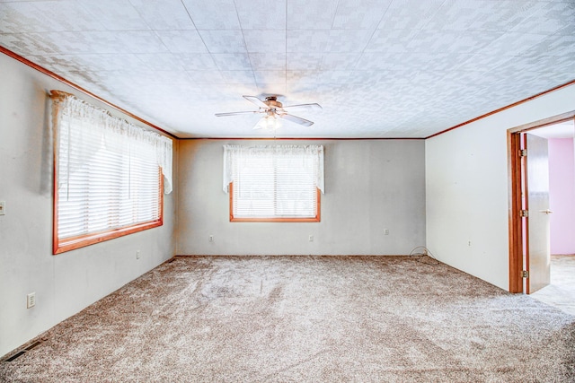 carpeted empty room featuring visible vents, crown molding, and ceiling fan