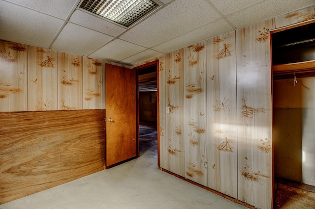 corridor featuring concrete floors, a drop ceiling, and wooden walls