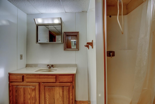 bathroom with a paneled ceiling, walk in shower, and vanity