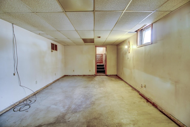 basement with a paneled ceiling and baseboards