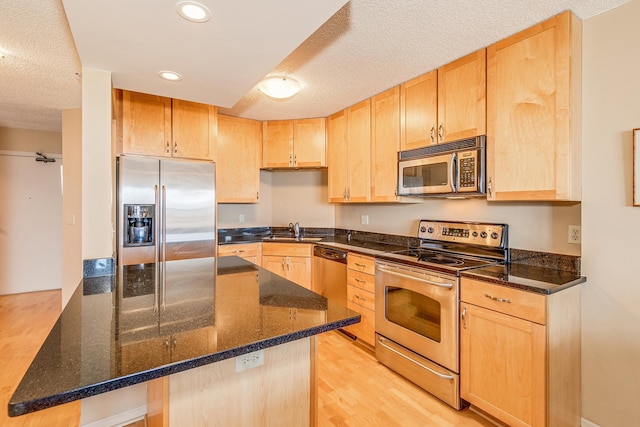 kitchen featuring stainless steel appliances, dark stone countertops, light brown cabinets, and sink