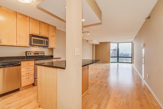 kitchen featuring light brown cabinets, stainless steel appliances, dark stone counters, light hardwood / wood-style floors, and expansive windows