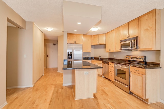 kitchen with light brown cabinetry, a textured ceiling, appliances with stainless steel finishes, and a kitchen island