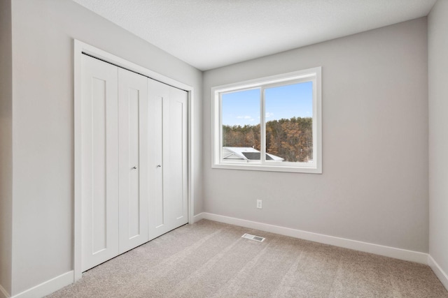 unfurnished bedroom featuring light carpet, a closet, and a textured ceiling