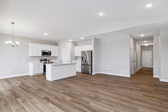 kitchen with stainless steel appliances, lofted ceiling, a center island with sink, white cabinets, and hardwood / wood-style flooring