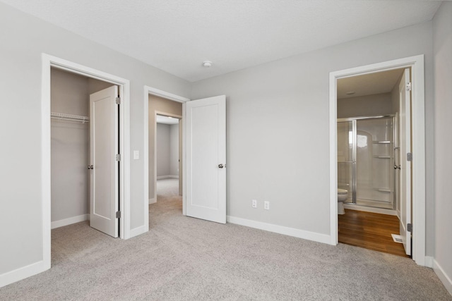 unfurnished bedroom with a closet, light colored carpet, a textured ceiling, and ensuite bath