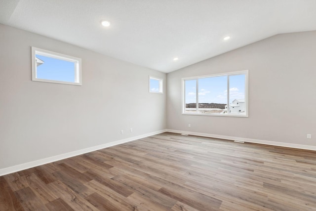 spare room featuring vaulted ceiling, a textured ceiling, and light hardwood / wood-style flooring