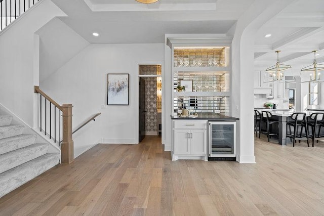 bar with pendant lighting, an inviting chandelier, light hardwood / wood-style floors, white cabinetry, and beverage cooler