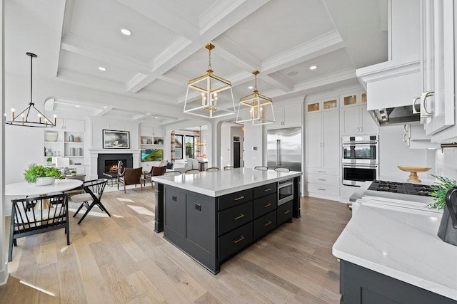 kitchen with white cabinets, pendant lighting, light wood-type flooring, and a center island with sink