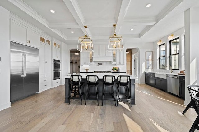 kitchen with appliances with stainless steel finishes, beam ceiling, a center island, light hardwood / wood-style floors, and white cabinetry