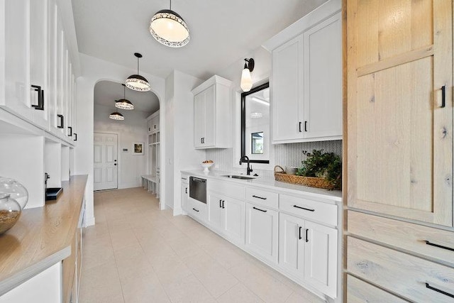 kitchen featuring decorative backsplash, sink, white cabinets, and hanging light fixtures