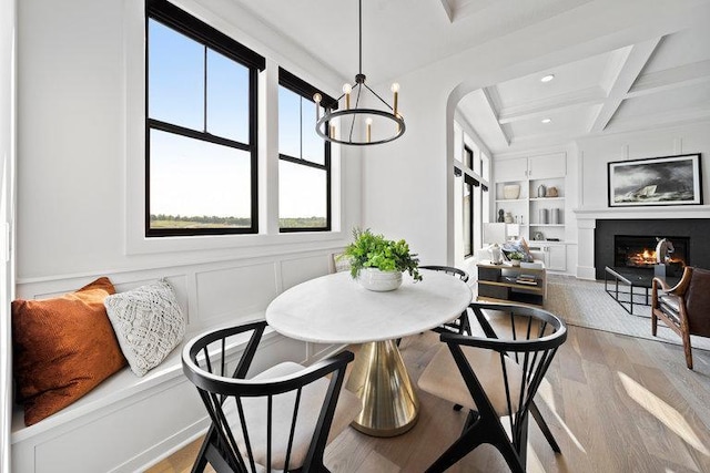 dining area with beam ceiling, coffered ceiling, built in features, a chandelier, and light hardwood / wood-style floors