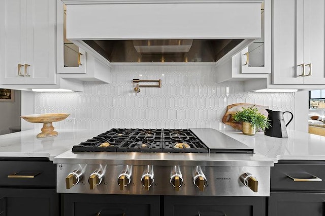 kitchen featuring light stone countertops, ventilation hood, backsplash, stainless steel gas stovetop, and white cabinets